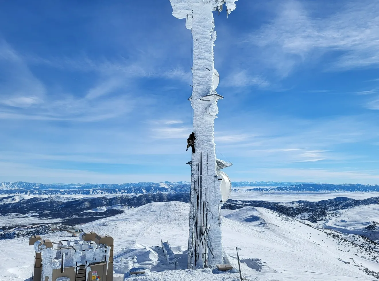 Climber ascending an ice-covered tower above snowy mountains