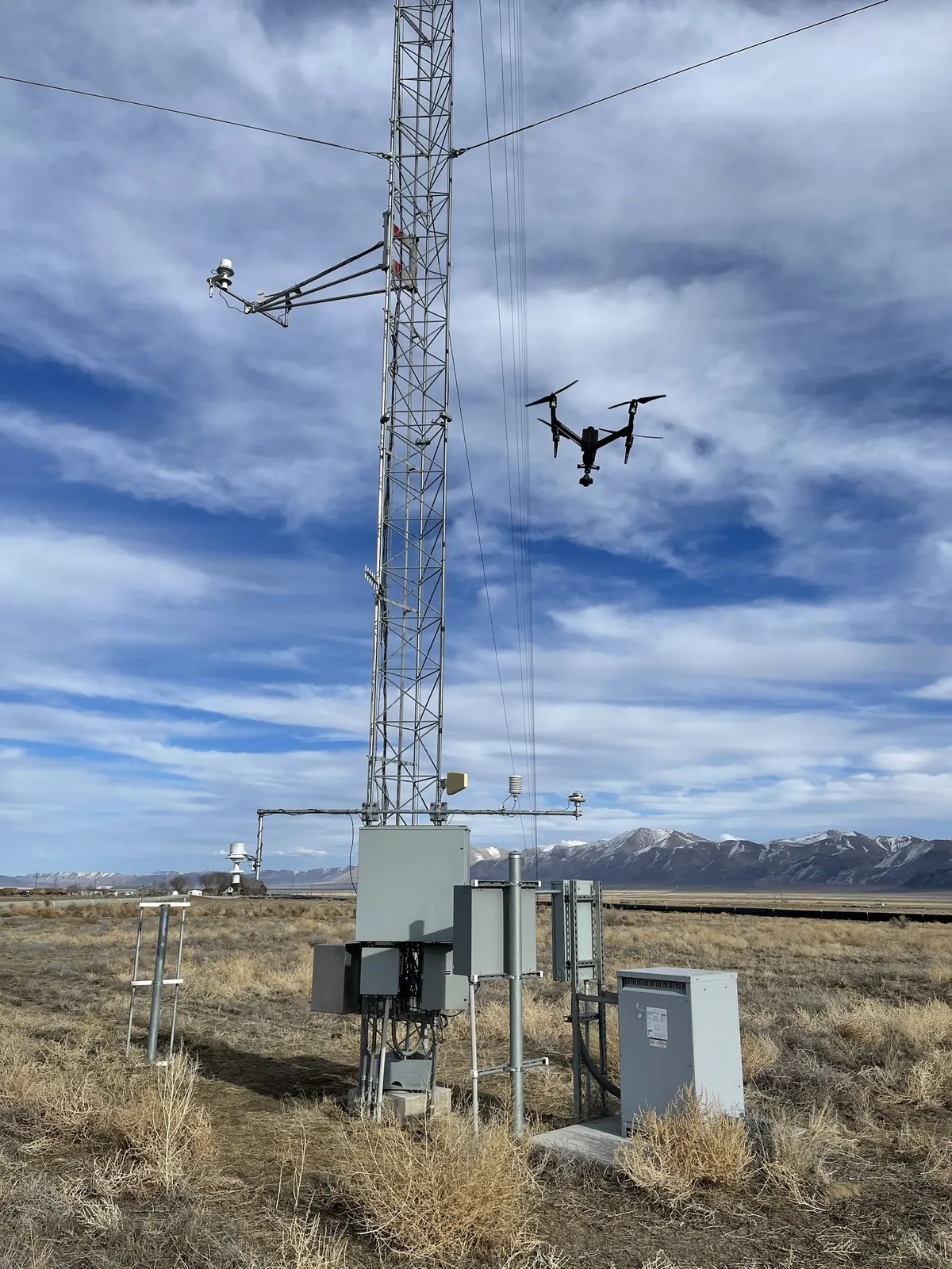 Drone inspecting a guyed tower and equipment cabinets