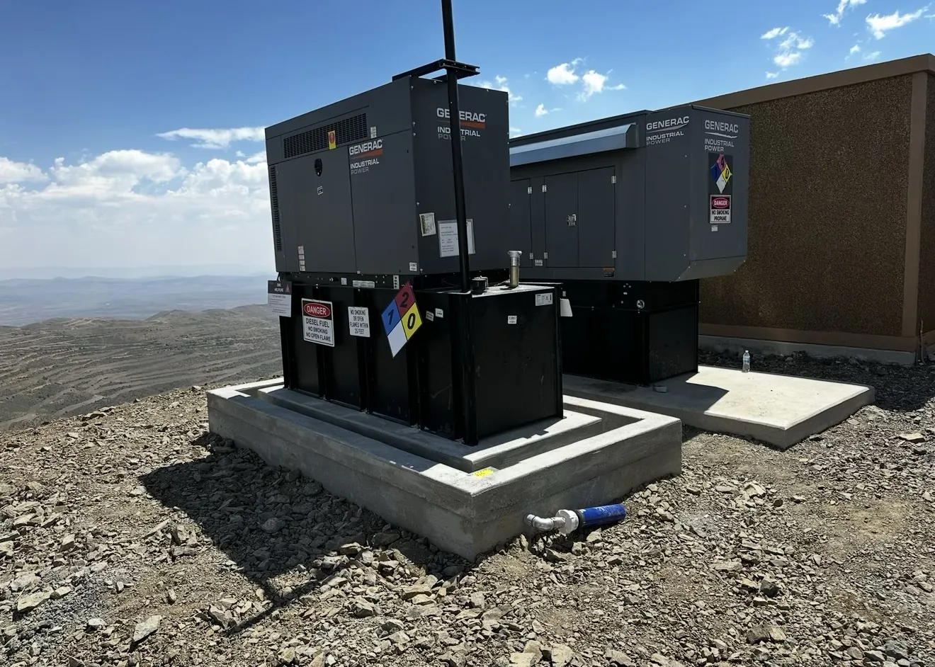 Two industrial generators set on new concrete foundations at a mountaintop site