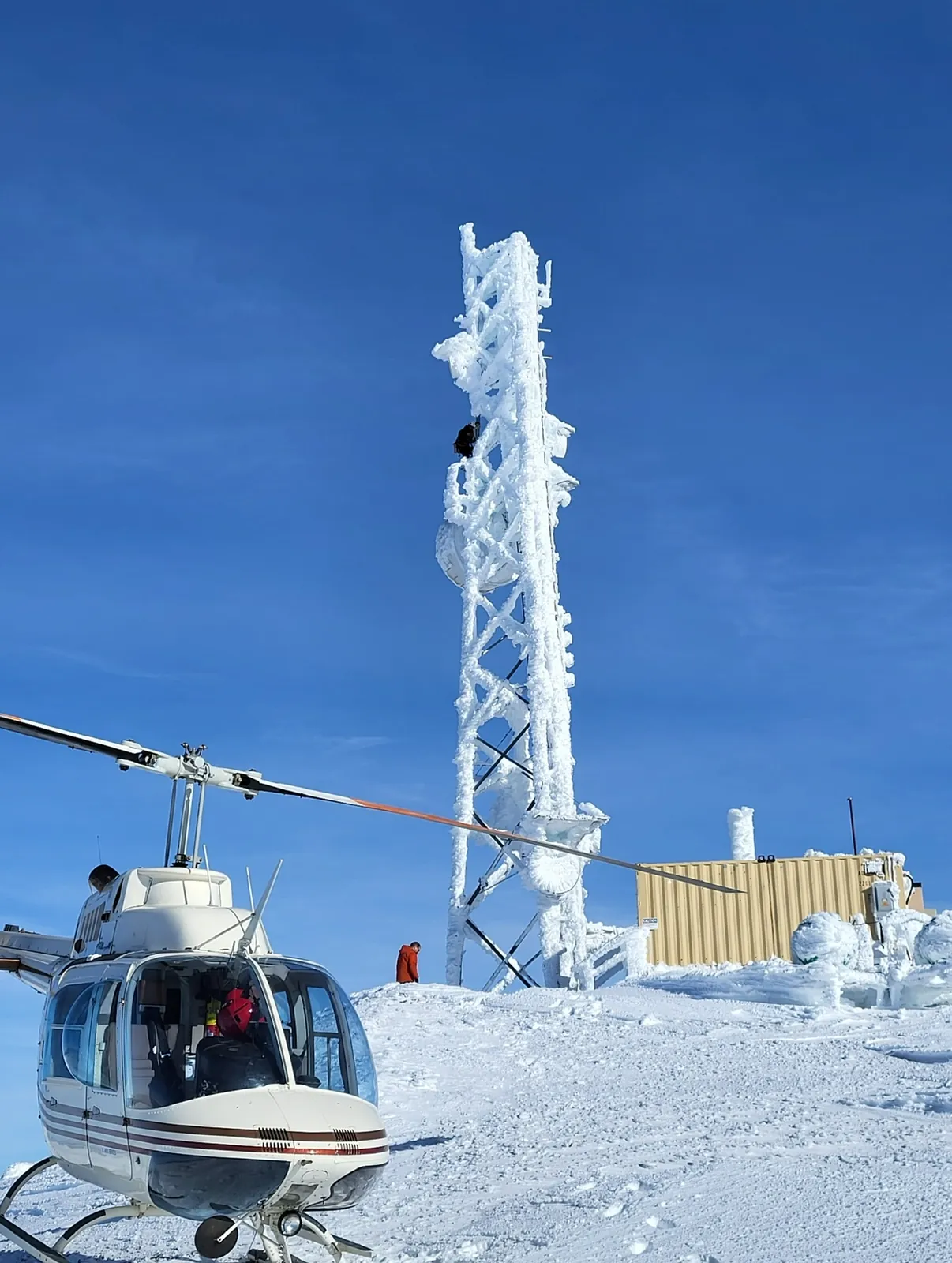 Helicopter landed beside an ice-covered tower on a snowy summit