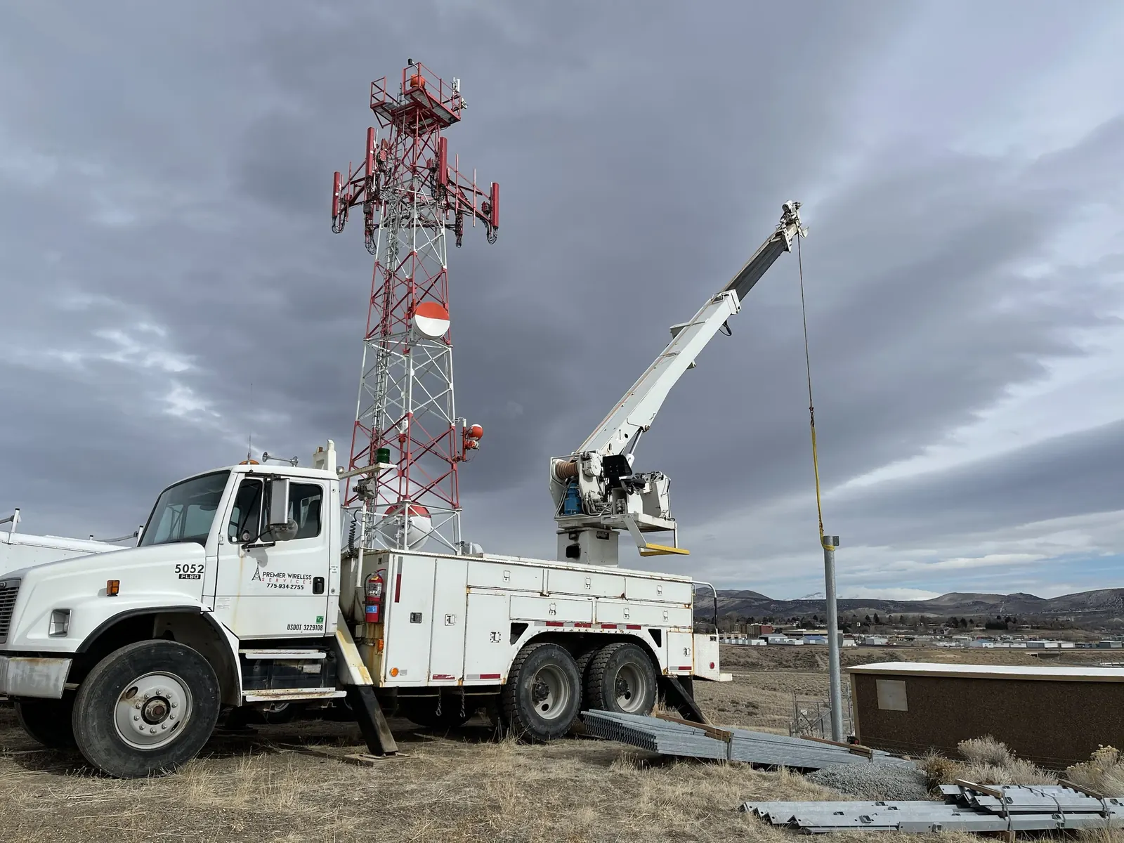 Premier Wireless Services boom truck beside a red and white lattice tower