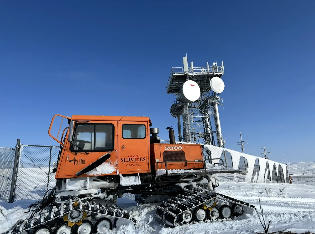 Premier Services snowcat parked beside a mountaintop tower in snow