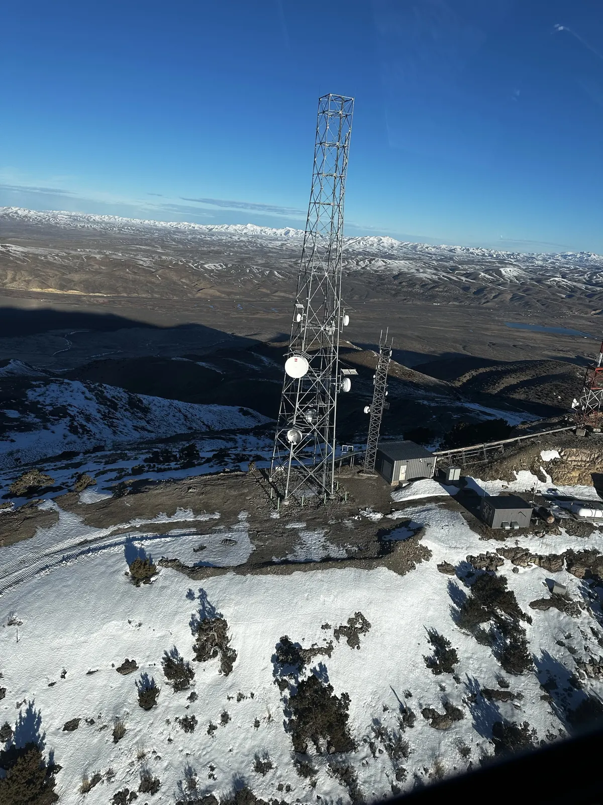 Aerial view of a snowy mountaintop lattice tower and shelters