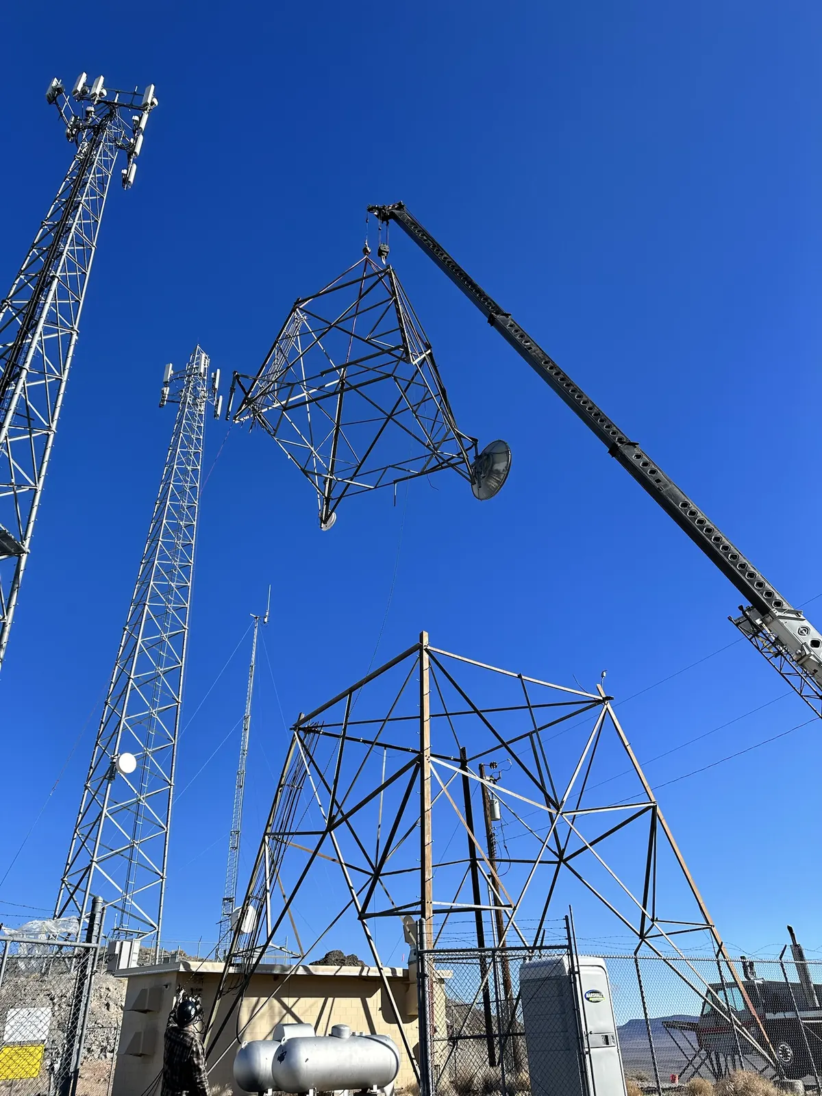 Crane lifting a lattice tower section beside other towers